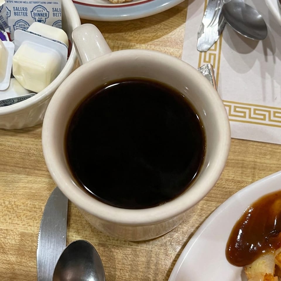 Coffee, butter packets, biscuits, and gravy-covered breakfast potatoes arranged on a wooden restaurant table.